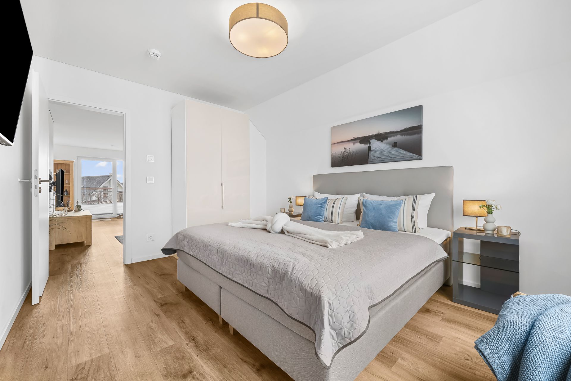 Helles Schlafzimmer mit Doppelbett, Nachttischen, Schrank und Bild an der Wand.