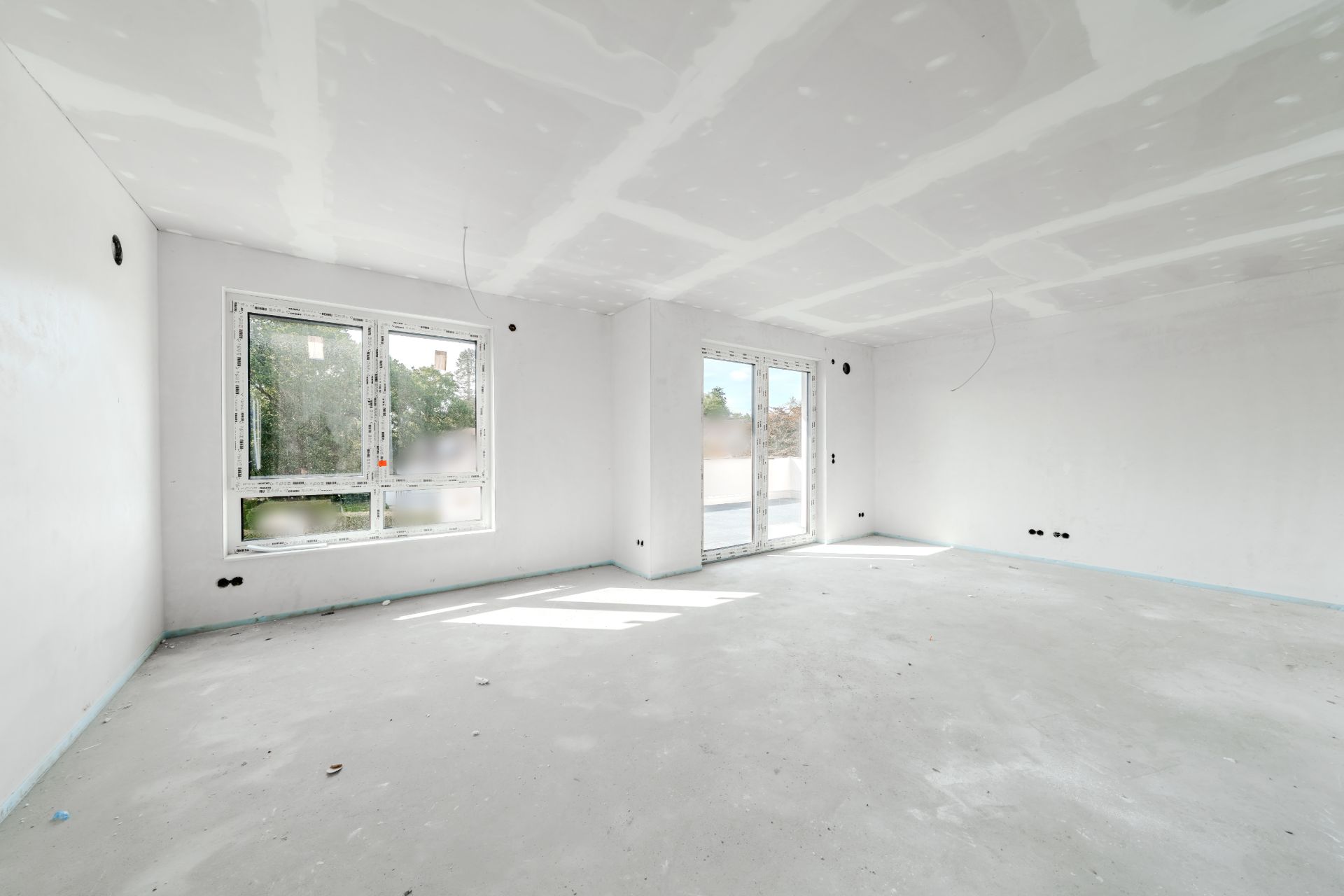Heller, leerer Raum mit zwei Fenstern und einer Glastür, Wände und Decke im Rohbau.