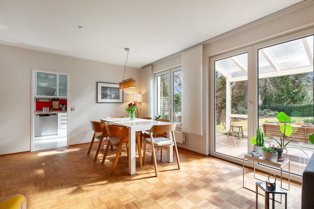 Helles Esszimmer mit Holzboden, großem Tisch, Stühlen und Zugang zur Terrasse mit Garten.