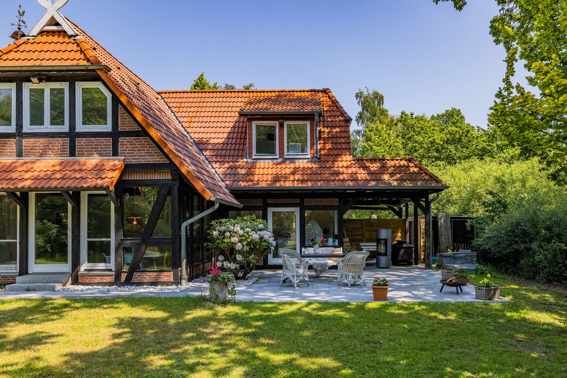 Fachwerkhaus mit Terrasse, Gartenmöbeln und Pflanzen im Garten bei sonnigem Wetter.