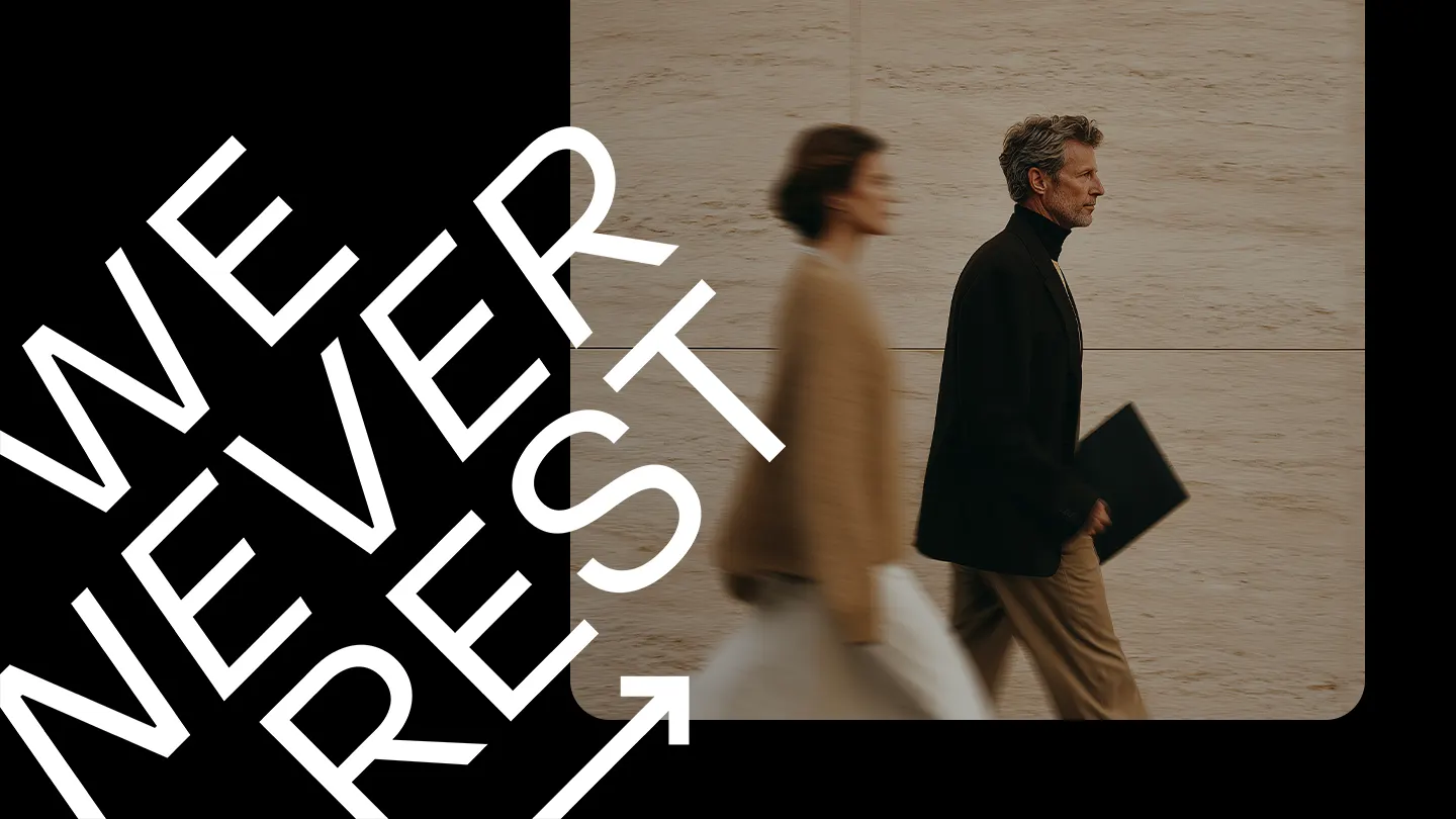 Zwei Personen gehen an einer hellen Wand vorbei, eine Schrift „WE NEVER REST“ ist im Vordergrund.