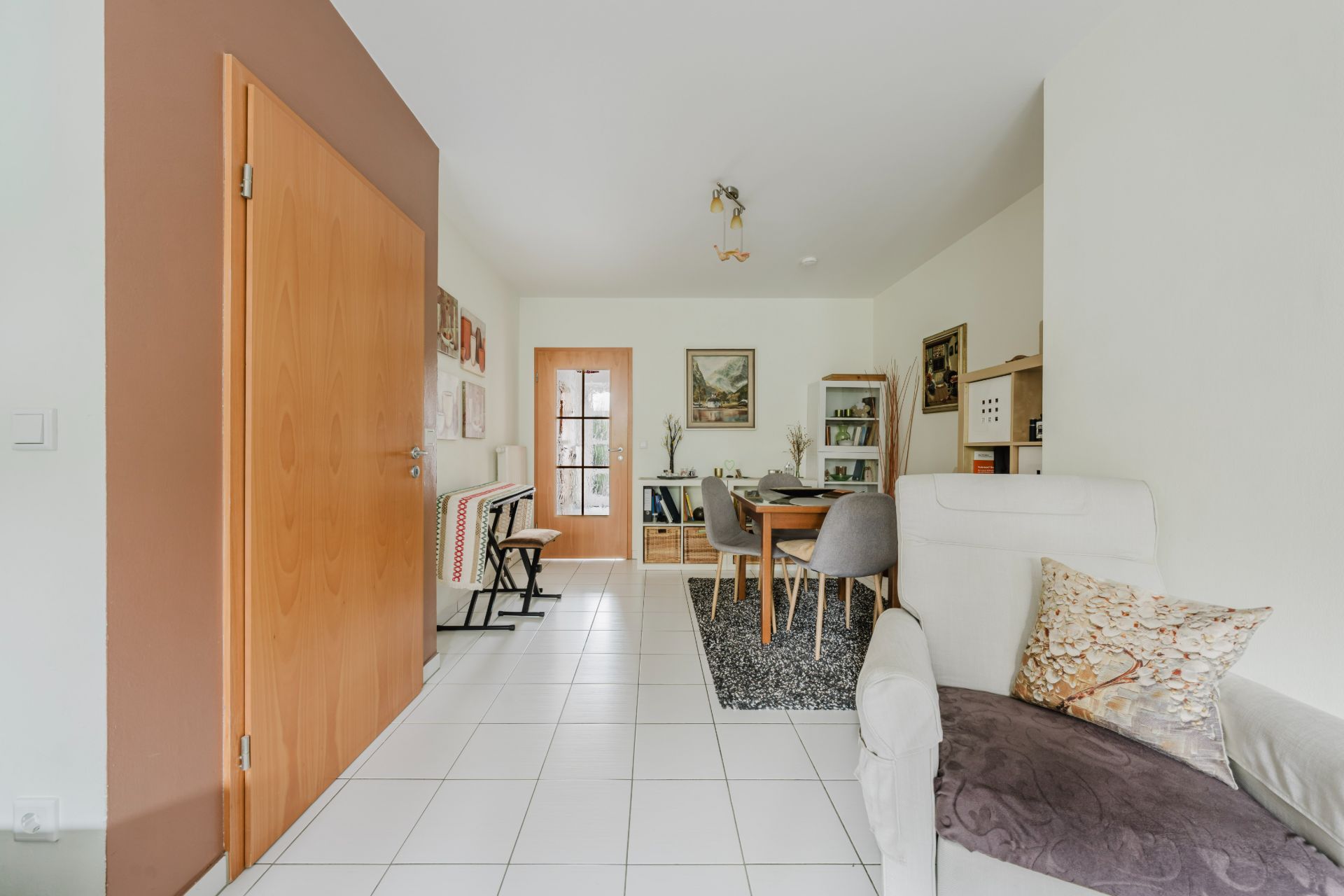 Helles Wohnzimmer mit Esstisch, Stühlen und weiß gefliestem Boden.