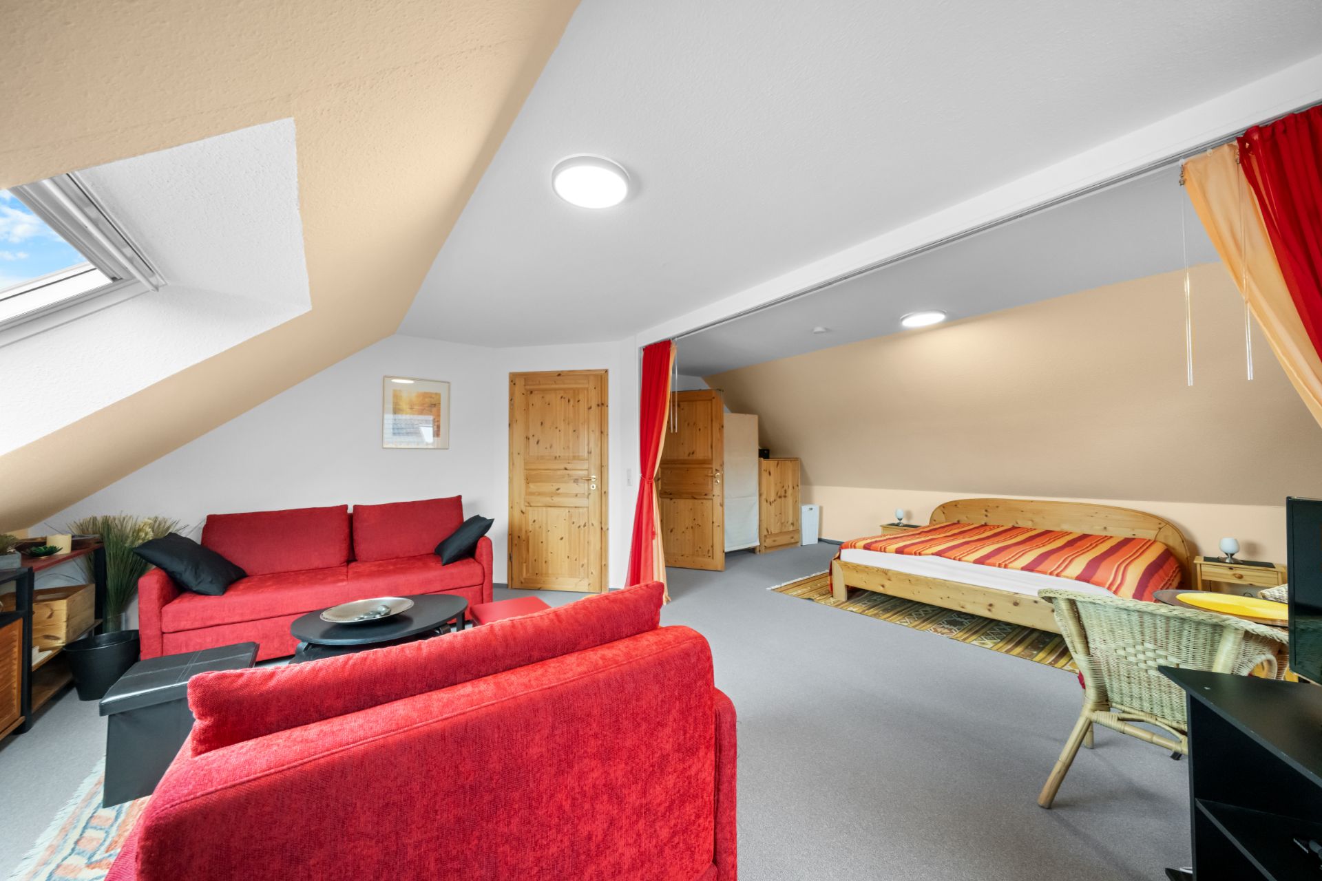 Dachzimmer mit zwei roten Sofas, Bett, Holzmöbeln und Dachfenster.