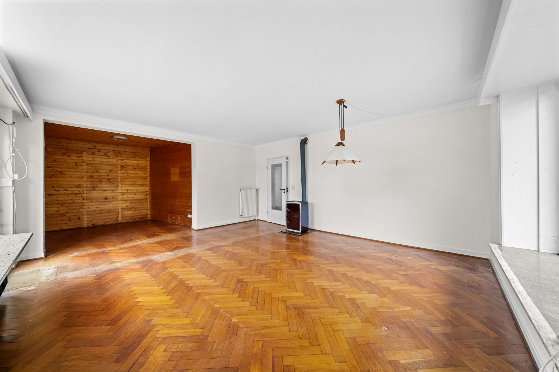 Leerer Raum mit Parkettboden, Holzofen und Holzvertäfelung an einer Wand.