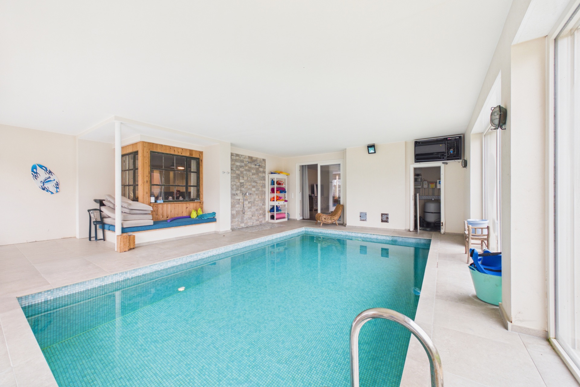 Heller Innenraum mit Swimmingpool, Sitzbereich und großen Fenstern.