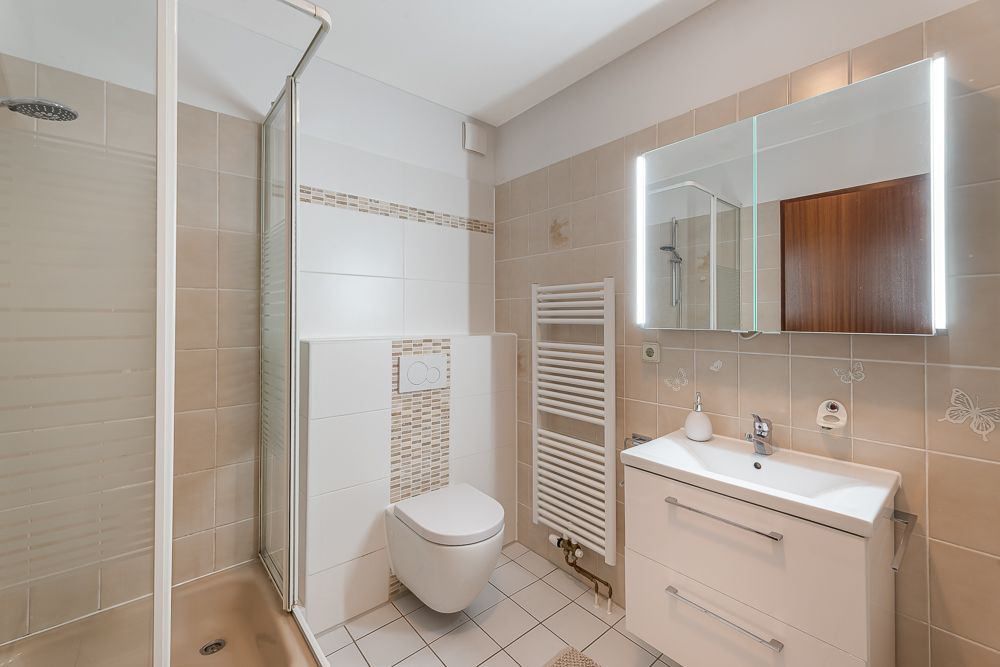 Modernes Badezimmer mit Dusche, Toilette, Waschbecken und beleuchtetem Spiegel.