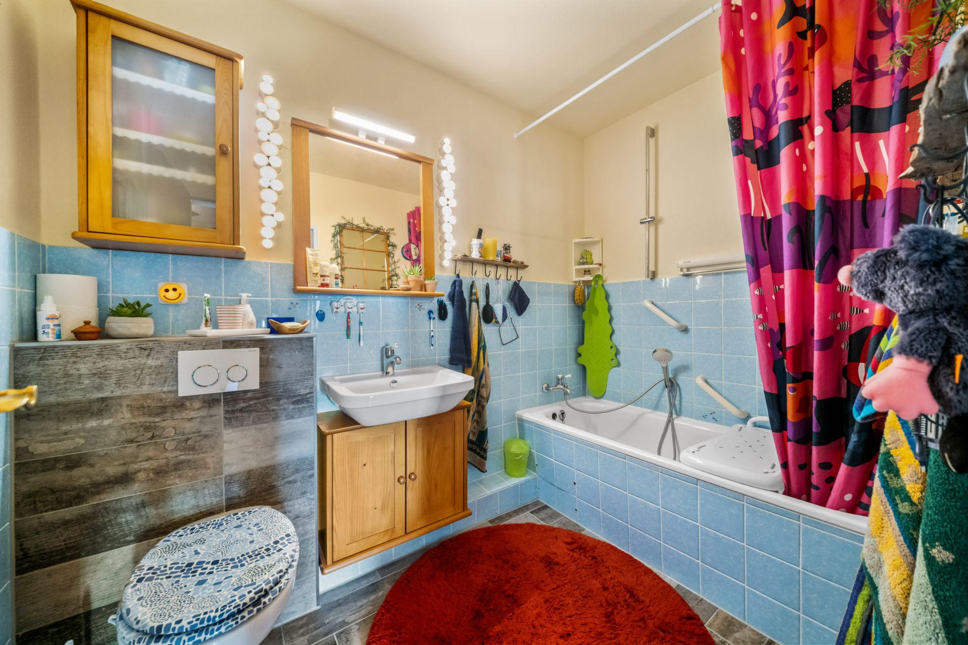 Badezimmer mit Badewanne, Waschbecken, WC, Holzschränken und bunter Duschvorhang.