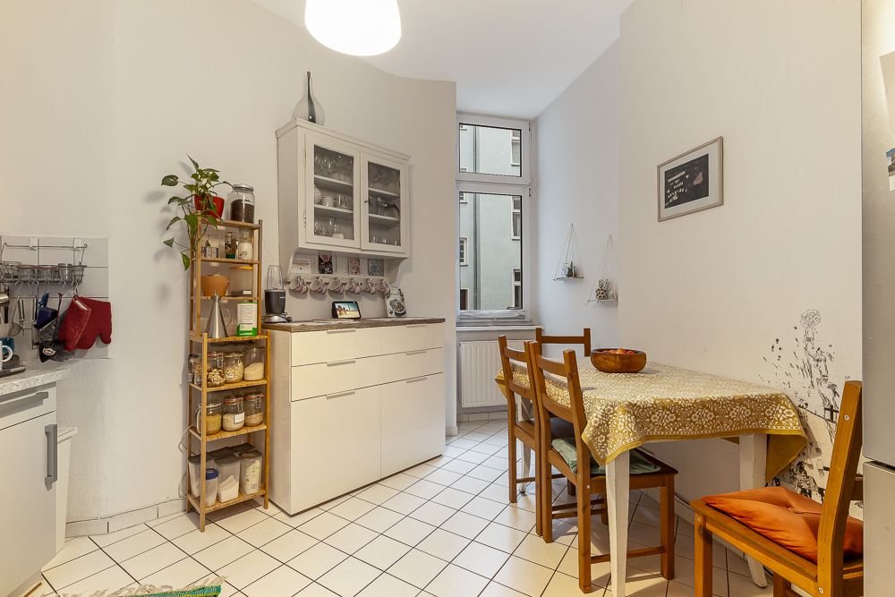 Helle Küche mit Esstisch, vier Stühlen, Regal, Schrank und Fenster.
