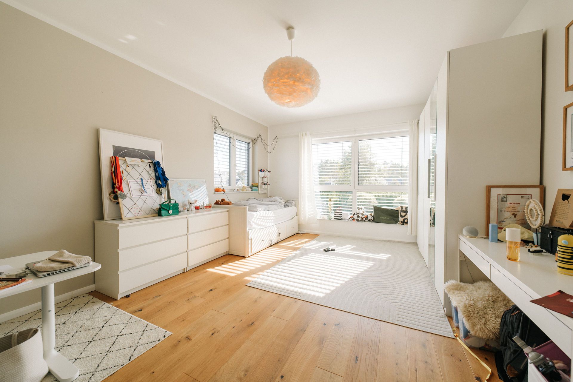 Helles Schlafzimmer mit Holzboden, großem Fenster, Bett, Kommode und Schreibtisch.