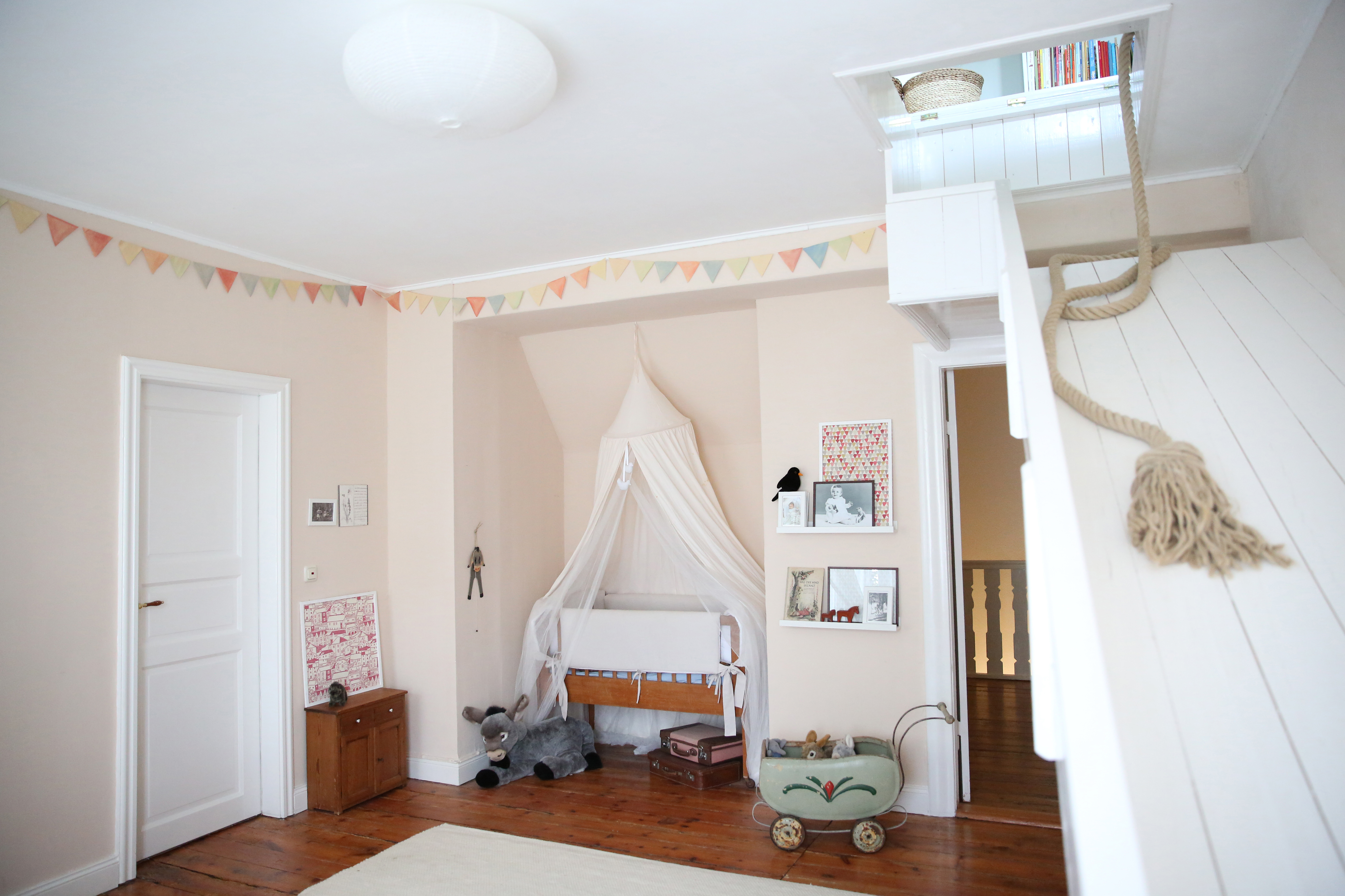 Helles Kinderzimmer mit Wiege, Stofftieren, Girlande und einer Holztreppe zu einem Hochbett.