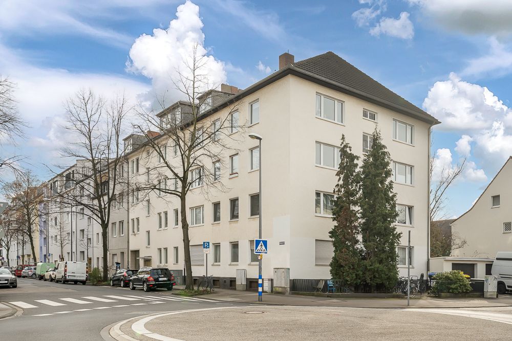 Mehrstöckiges Wohnhaus an einer Straßenecke mit parkenden Autos und Bäumen.