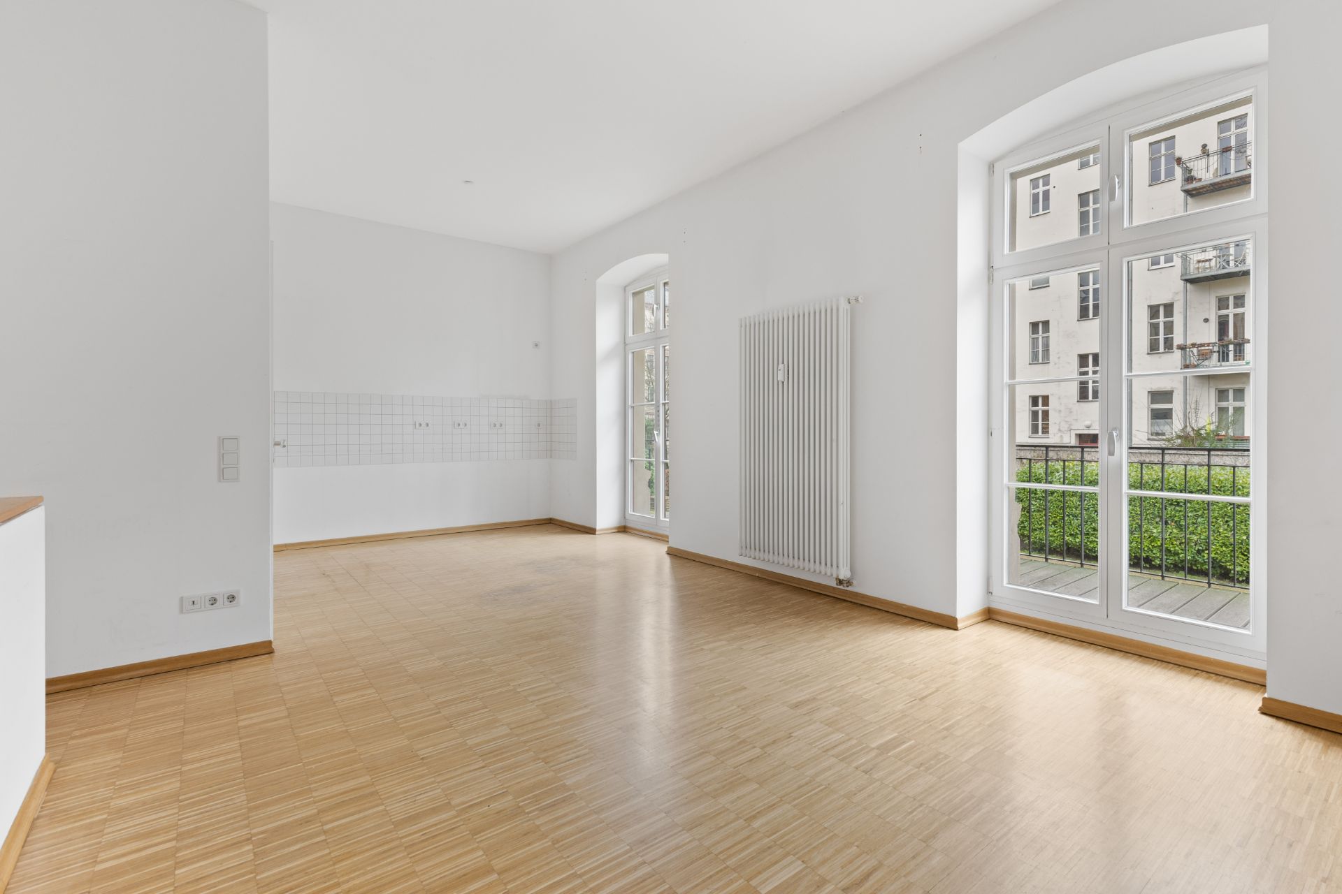 Heller leerer Raum mit Parkettboden, weißen Wänden und großen Fenstern mit Blick nach draußen.