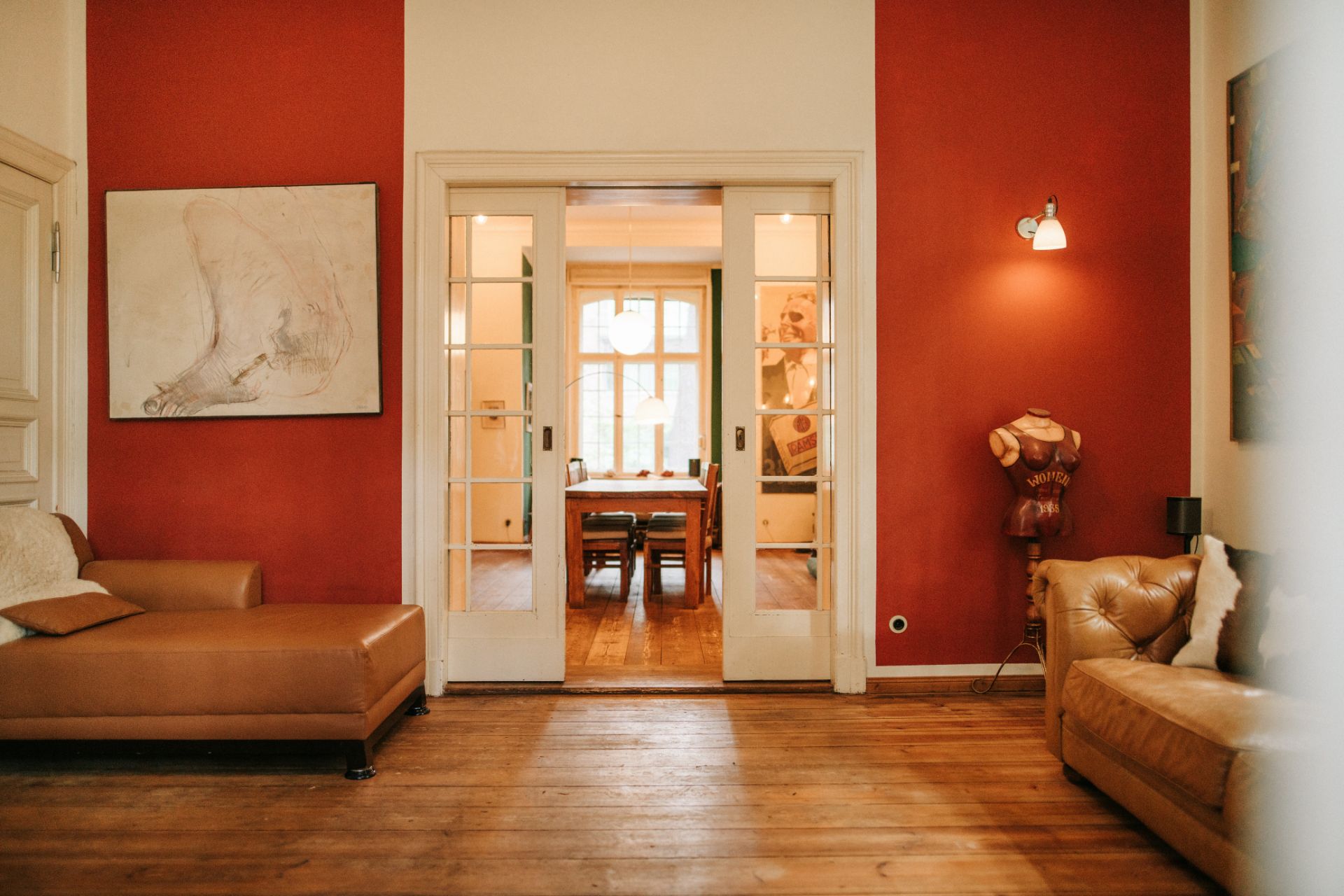 Wohnzimmer mit roten Wänden, Ledersofas und Glastüren zu einem Esszimmer mit großem Fenster.