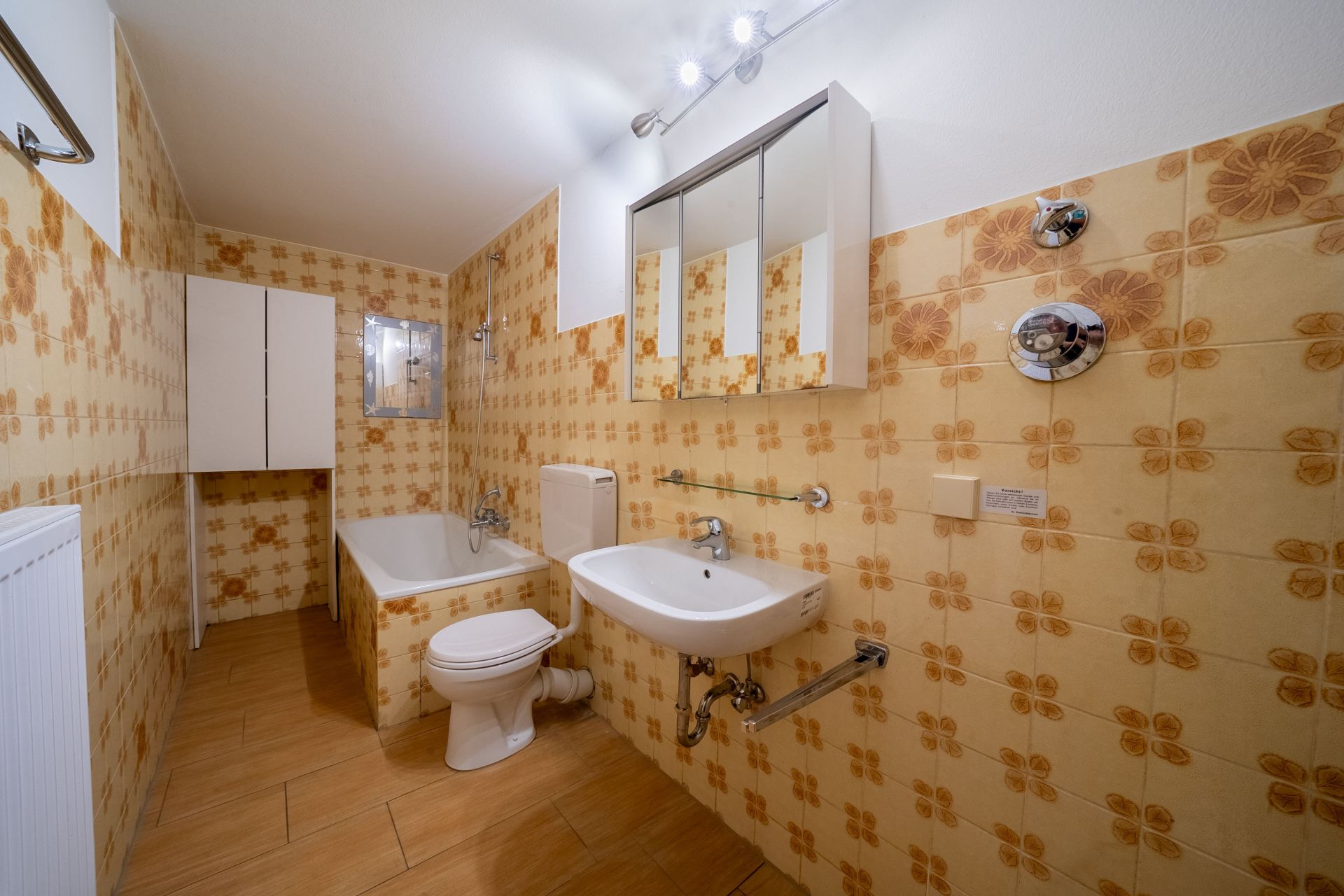 Badezimmer mit Badewanne, Toilette, Waschbecken und gemusterten Fliesen an den Wänden.