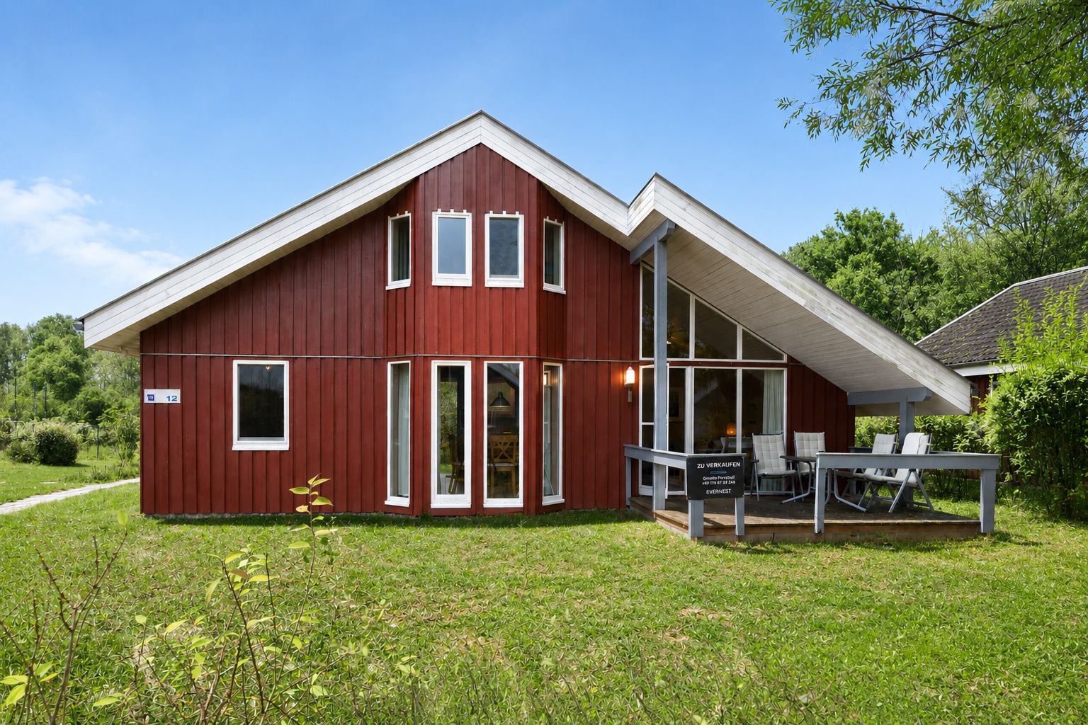 Rotes Holzhaus mit Terrasse und großen Fenstern im Garten.