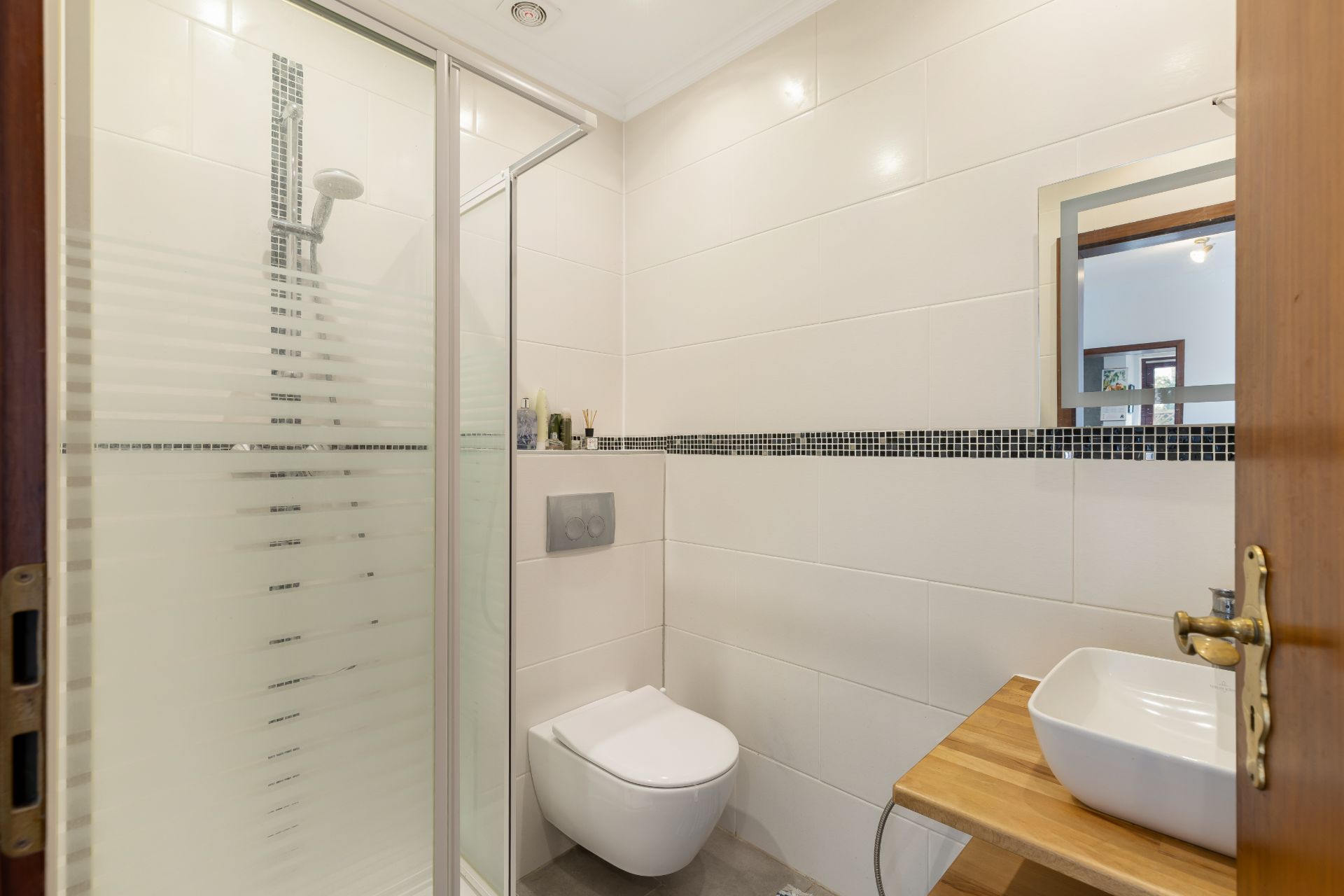 Modernes Badezimmer mit Dusche, Wandtoilette und Waschbecken auf Holztisch.