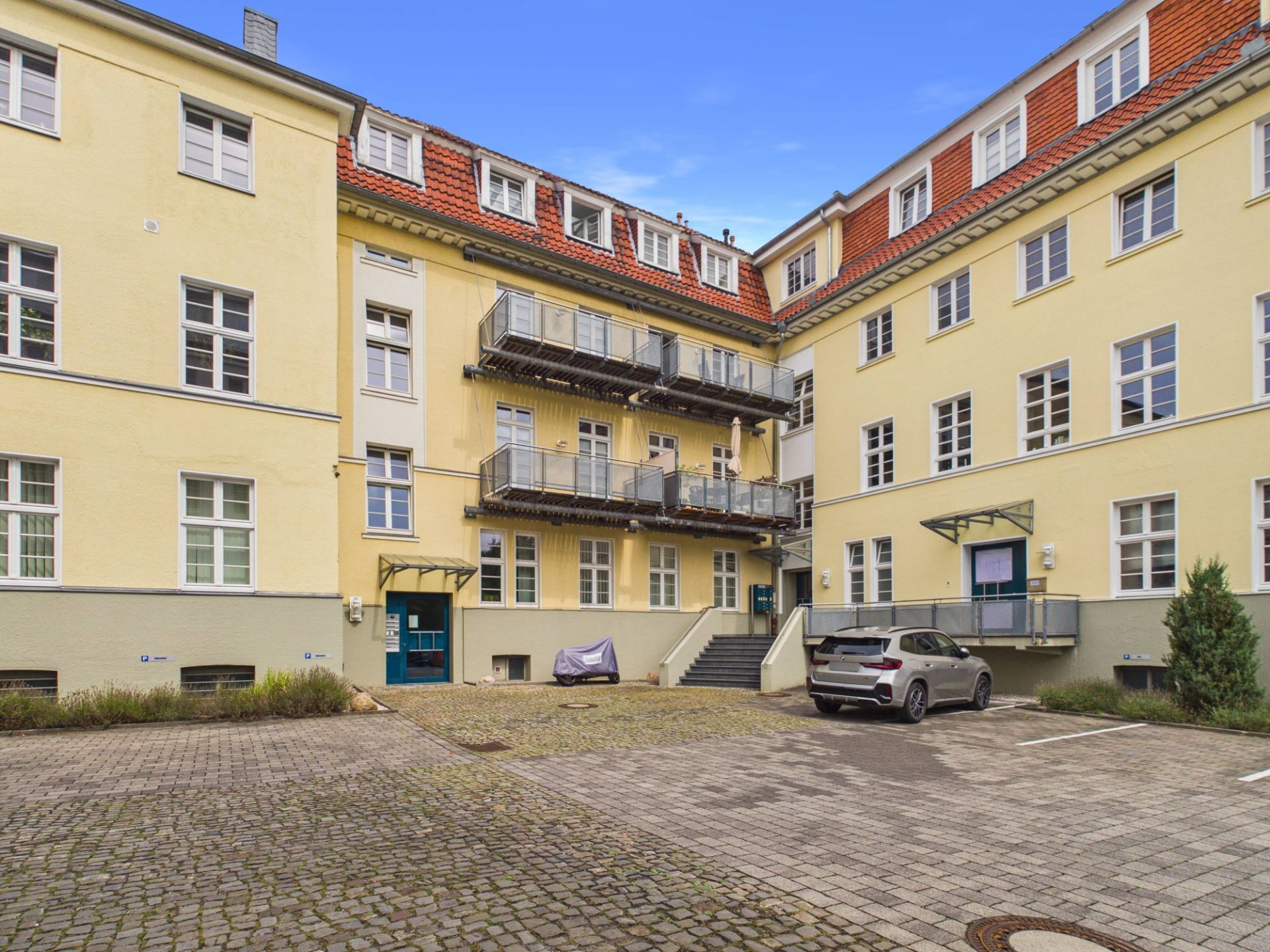 Innenhof eines gelben Wohngebäudes mit Balkonen, Parkplatz und geparktem Auto.