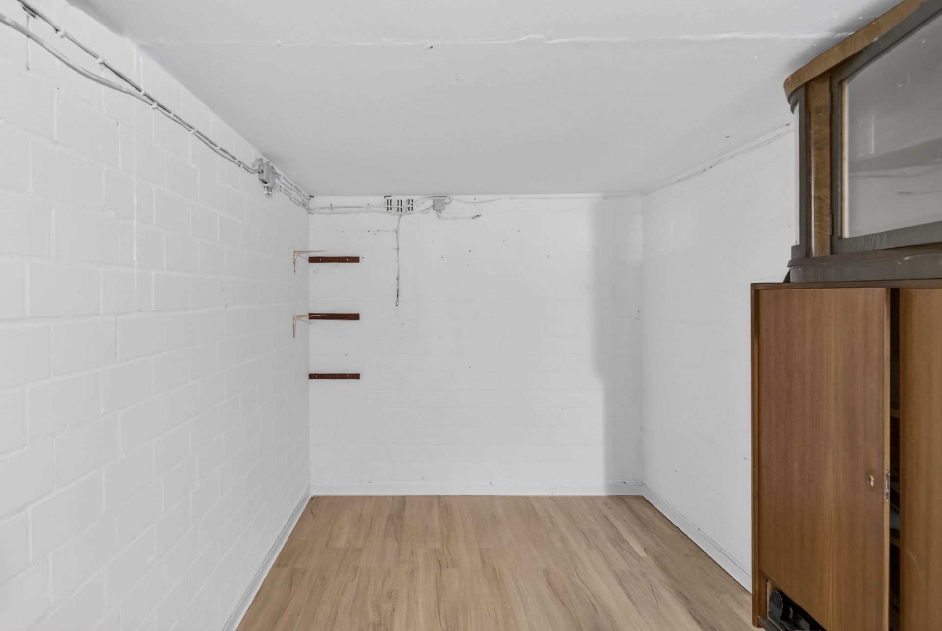 Kleiner Raum mit weißen Wänden, Holzboden und einem Holzschrank rechts.