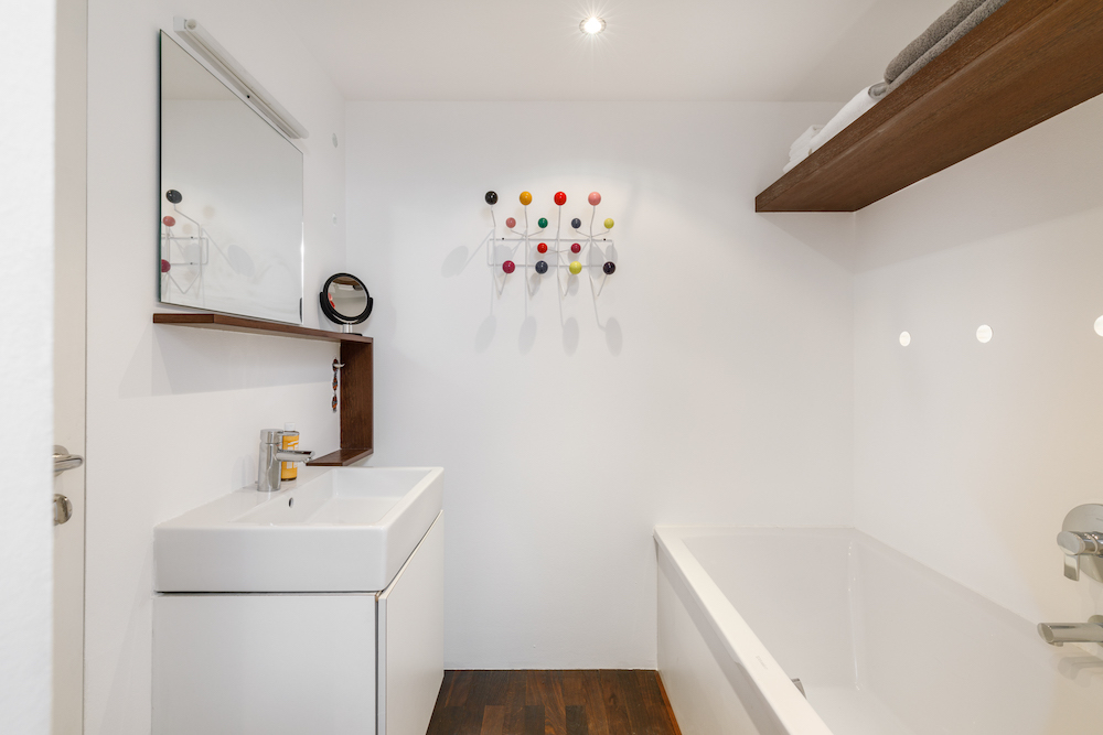 Modernes Badezimmer mit Badewanne, Waschbecken, Wandspiegel und bunter Garderobe an der Wand.