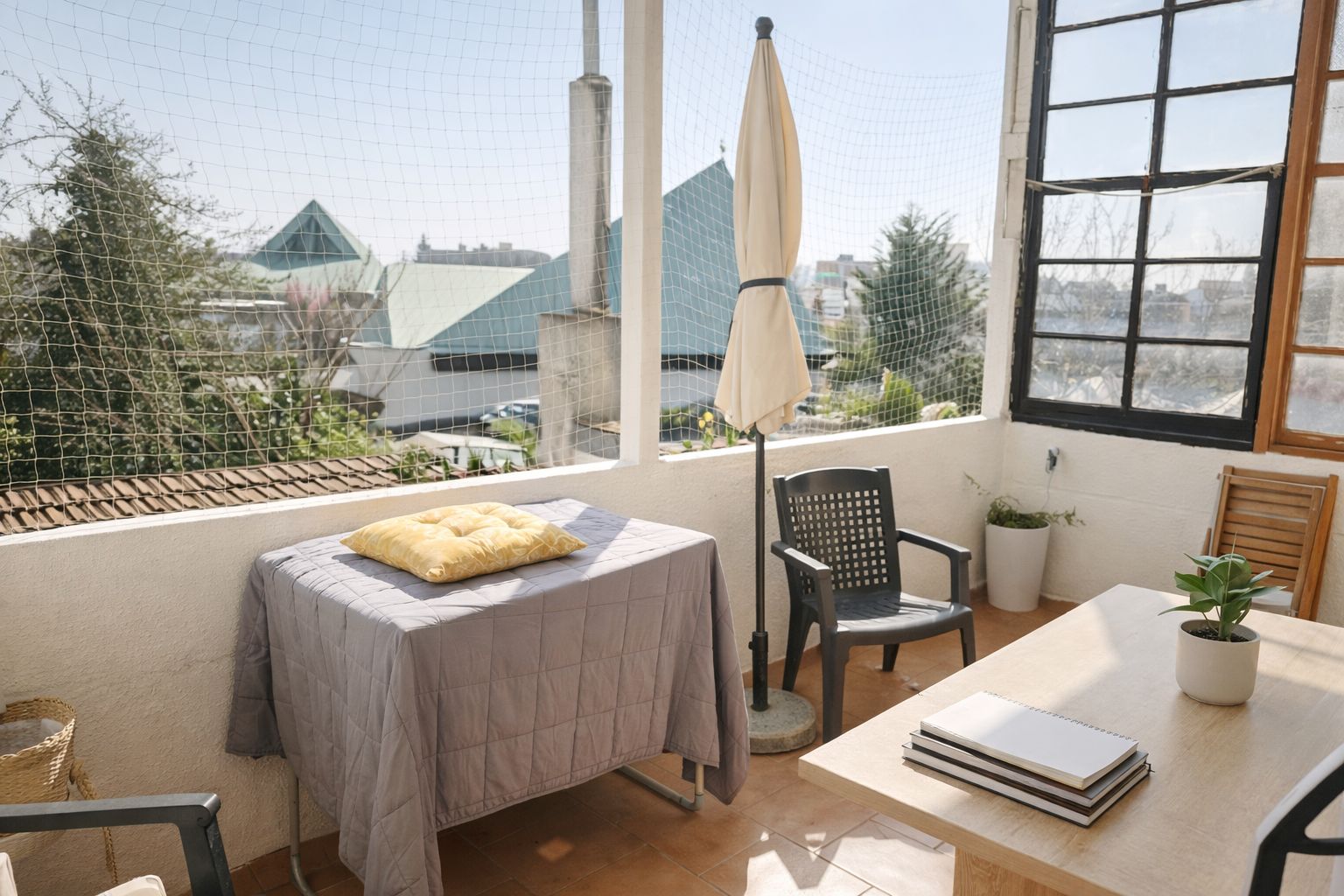 Heller Balkon mit Tisch, Stühlen, Sonnenschirm und Pflanzen, Ausblick auf Dächer und Bäume.