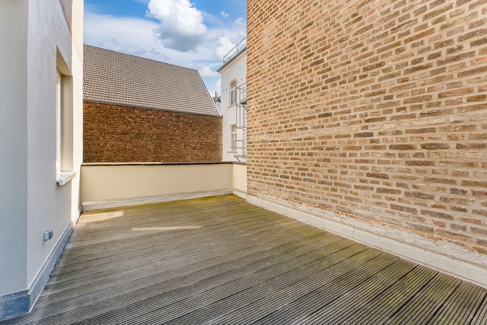 Große, leere Terrasse mit Holzboden und Backsteinwand, umgeben von Gebäuden.