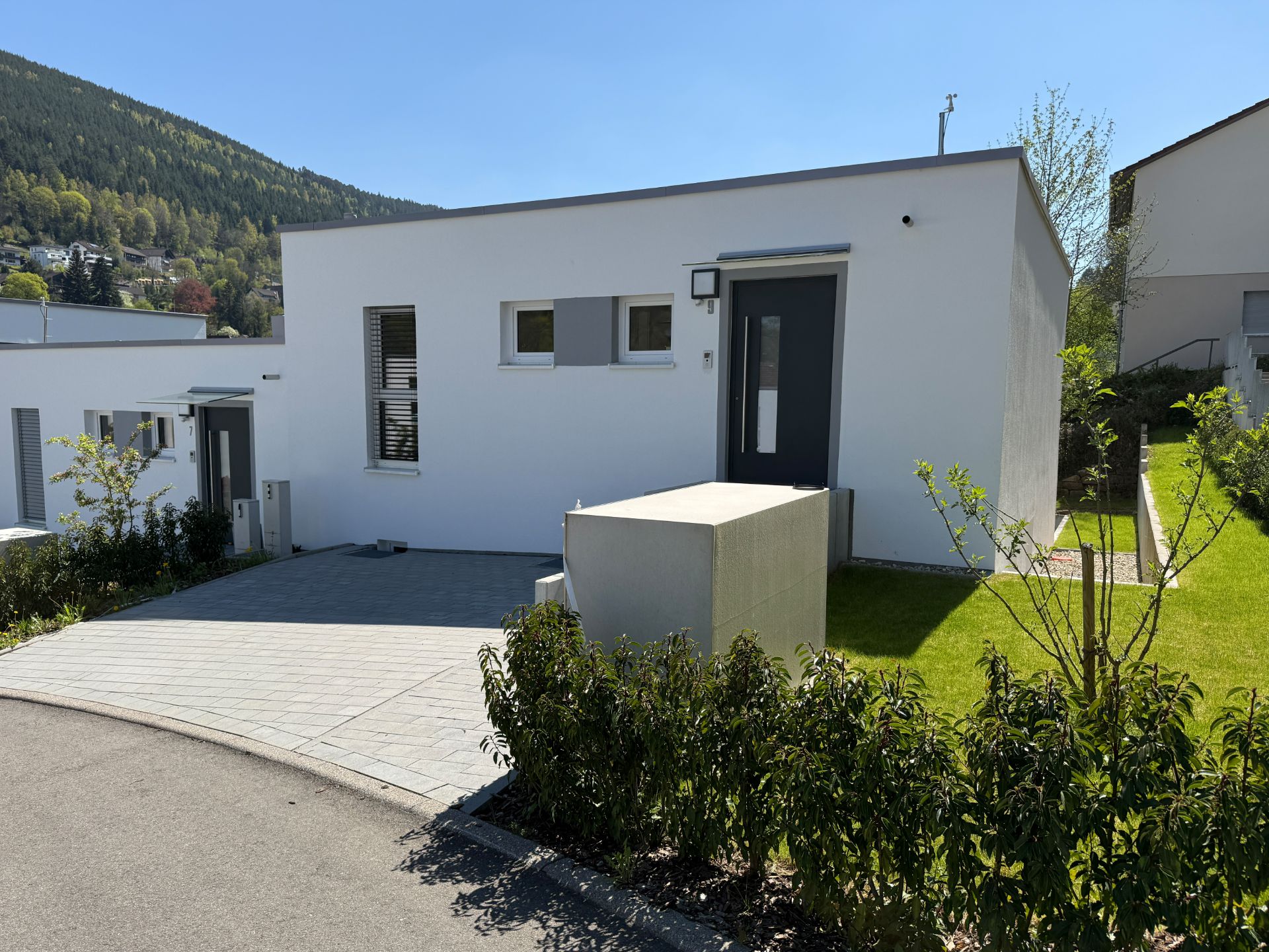 Modernes, einstöckiges weißes Haus mit Flachdach, Garten und Einfahrt an sonnigem Tag.