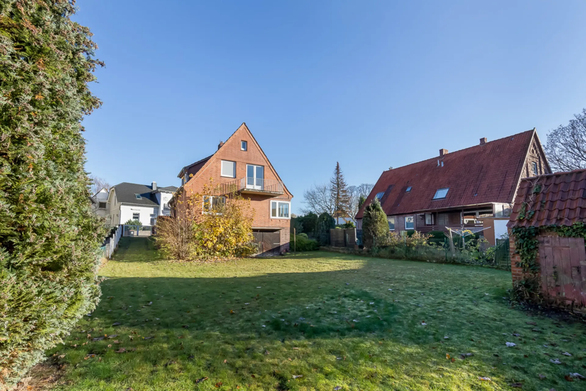 Backstein-Einfamilienhaus mit großem Garten und Rasenfläche, umgeben von anderen Häusern.
