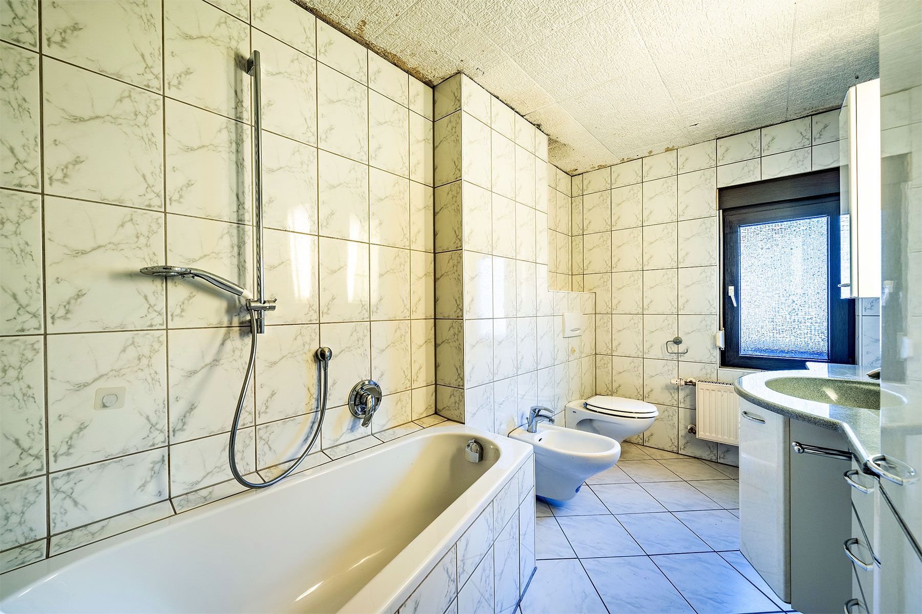 Helles Badezimmer mit Badewanne, Bidet, Toilette, Waschbecken und Fenster.