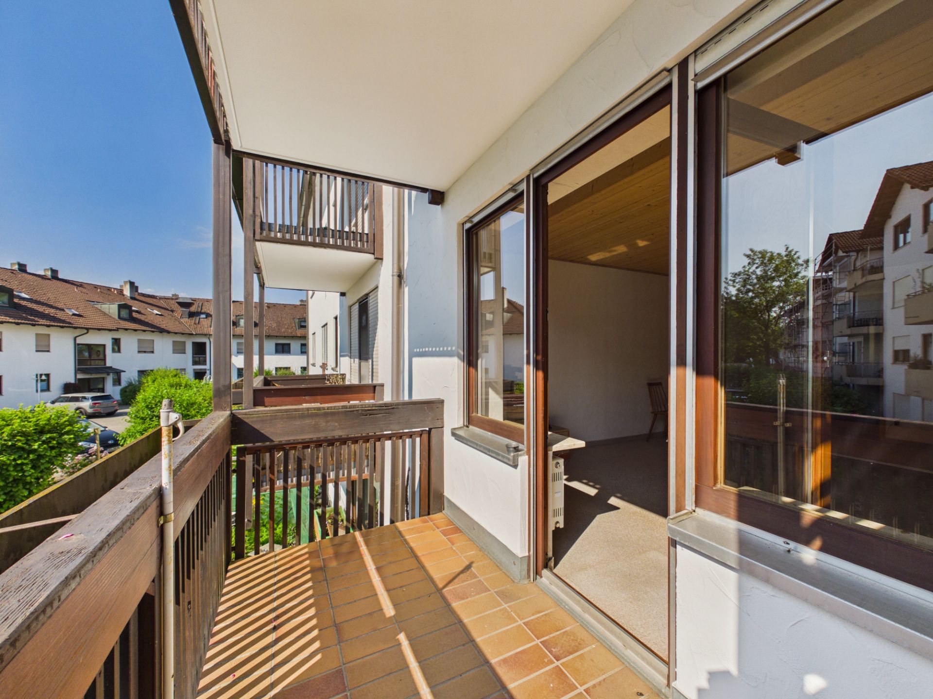Balkon mit Holzgitter und Fliesenboden, Zugang zu einem hellen Zimmer.