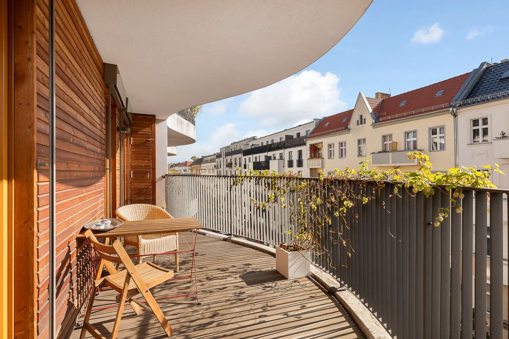 Großer Balkon mit Holzverkleidung, zwei Stühlen, Tisch und Blick auf Nachbarhäuser.