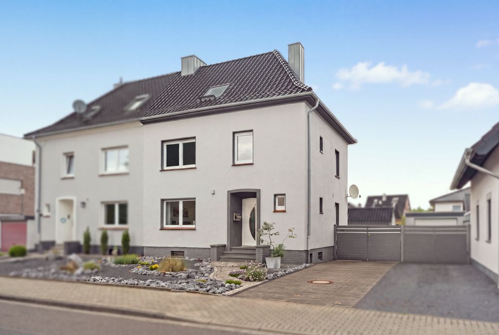 Modernes, weißes Doppelhaus mit gepflegtem Vorgarten und Einfahrt in einer Wohnstraße.