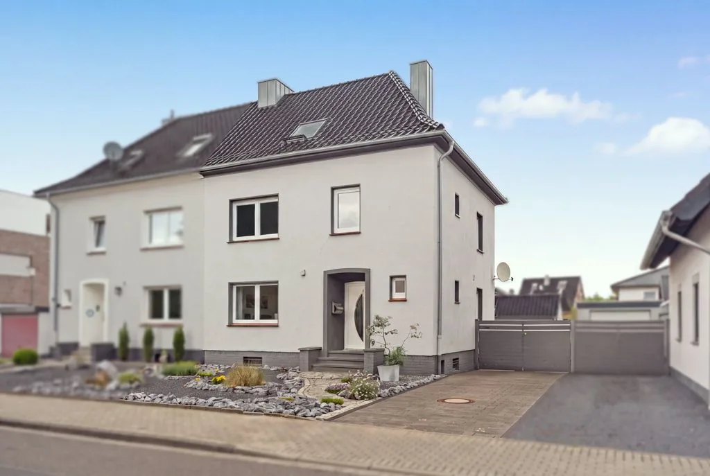 Modernes, weißes Doppelhaus mit gepflegtem Vorgarten und Einfahrt in einer Wohnstraße.