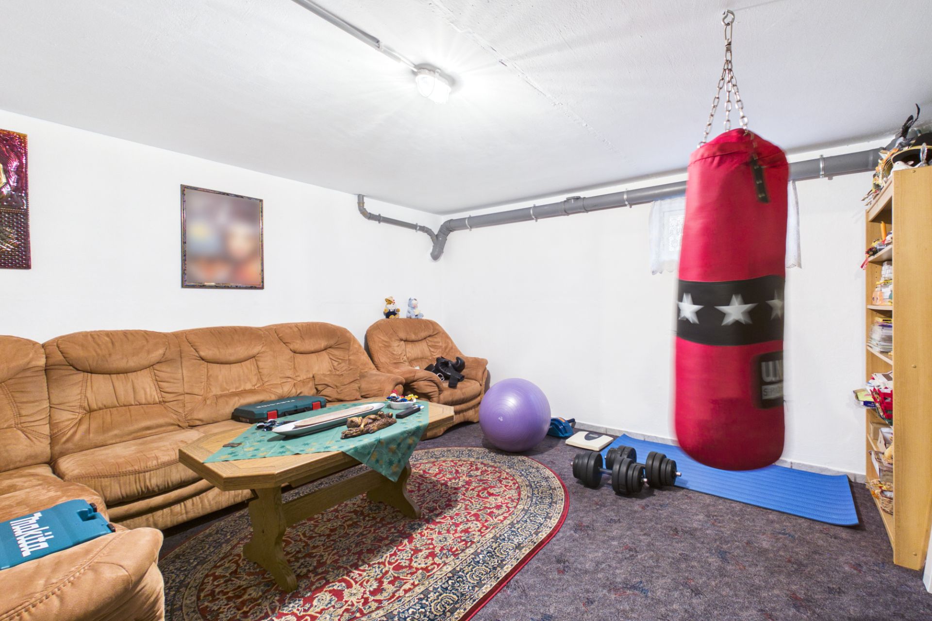 Wohnzimmer mit braunem Sofa, Teppich, Tisch, Boxsack, Hanteln und Gymnastikball.