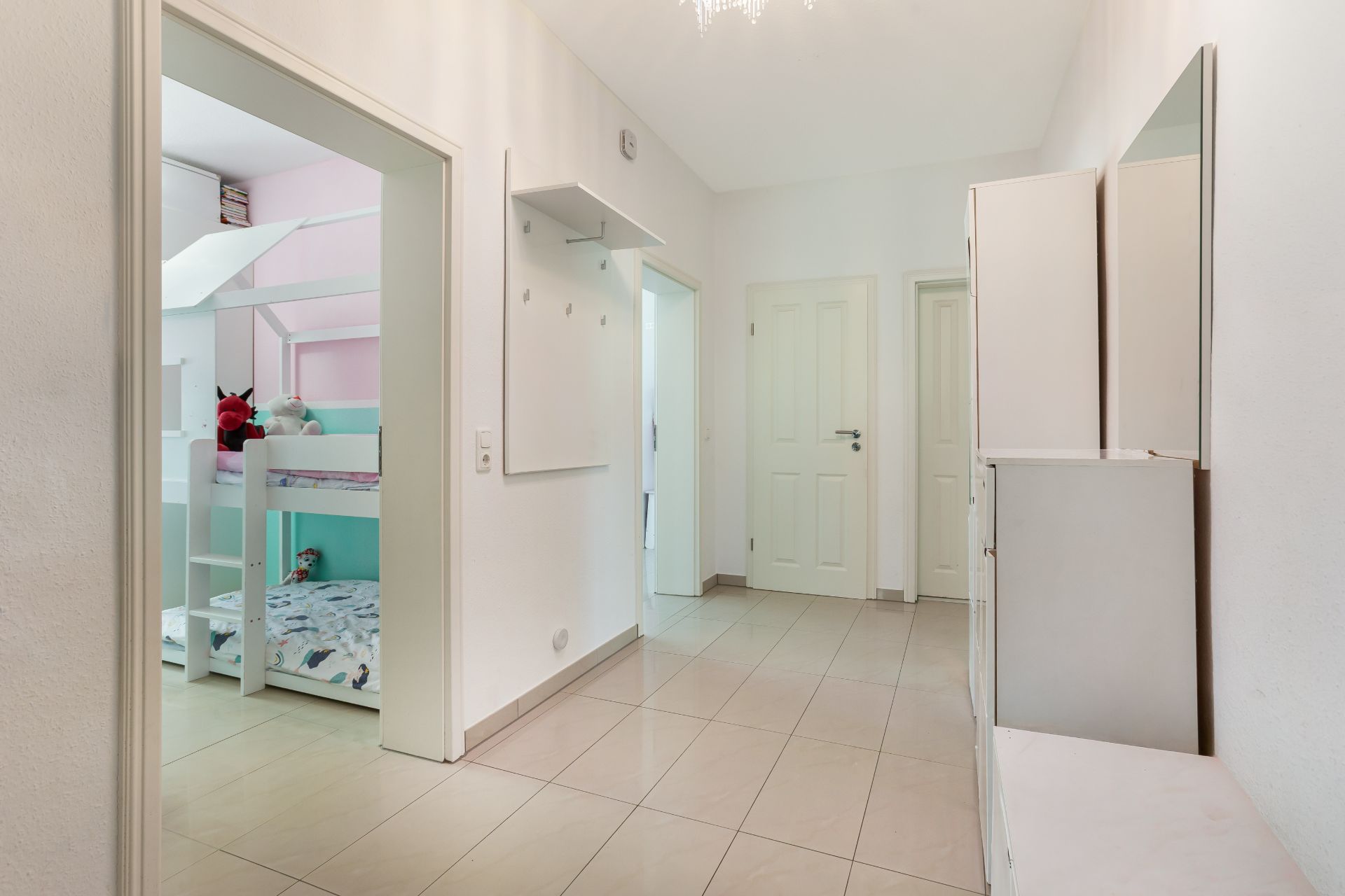 Heller Flur mit Fliesenboden, Garderobe und Blick in ein Kinderzimmer mit Etagenbett.