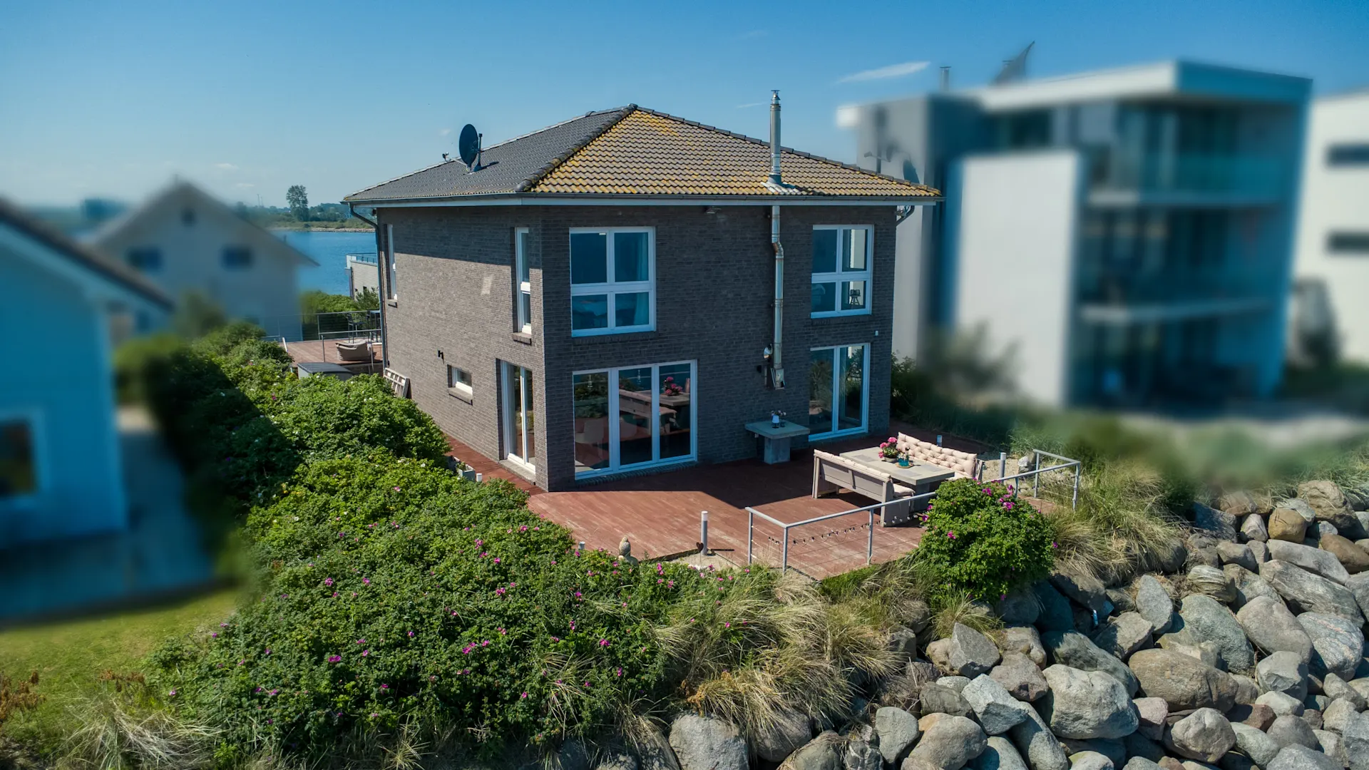 Modernes zweistöckiges Haus mit großer Terrasse und Garten, direkt an einem Gewässer.