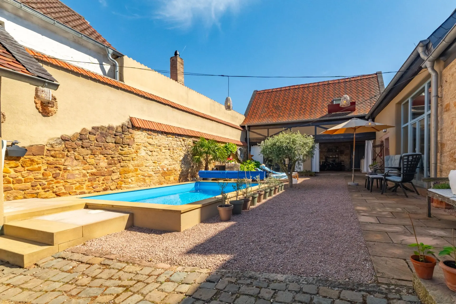 Innenhof mit kleinem Pool, Sonnenliegen, Topfpflanzen, Sitzbereich und Sonnenschirm.