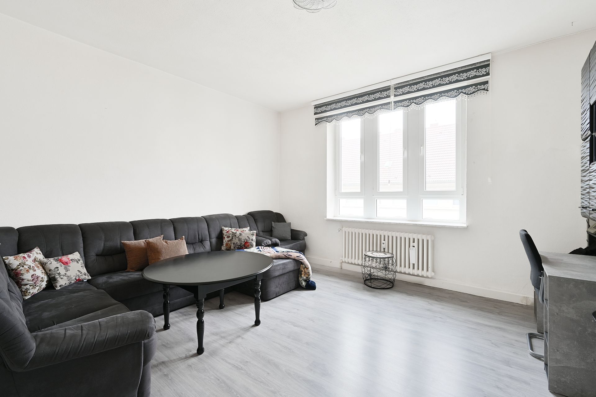 Helles Wohnzimmer mit schwarzem Ecksofa, Couchtisch und großen Fenstern.