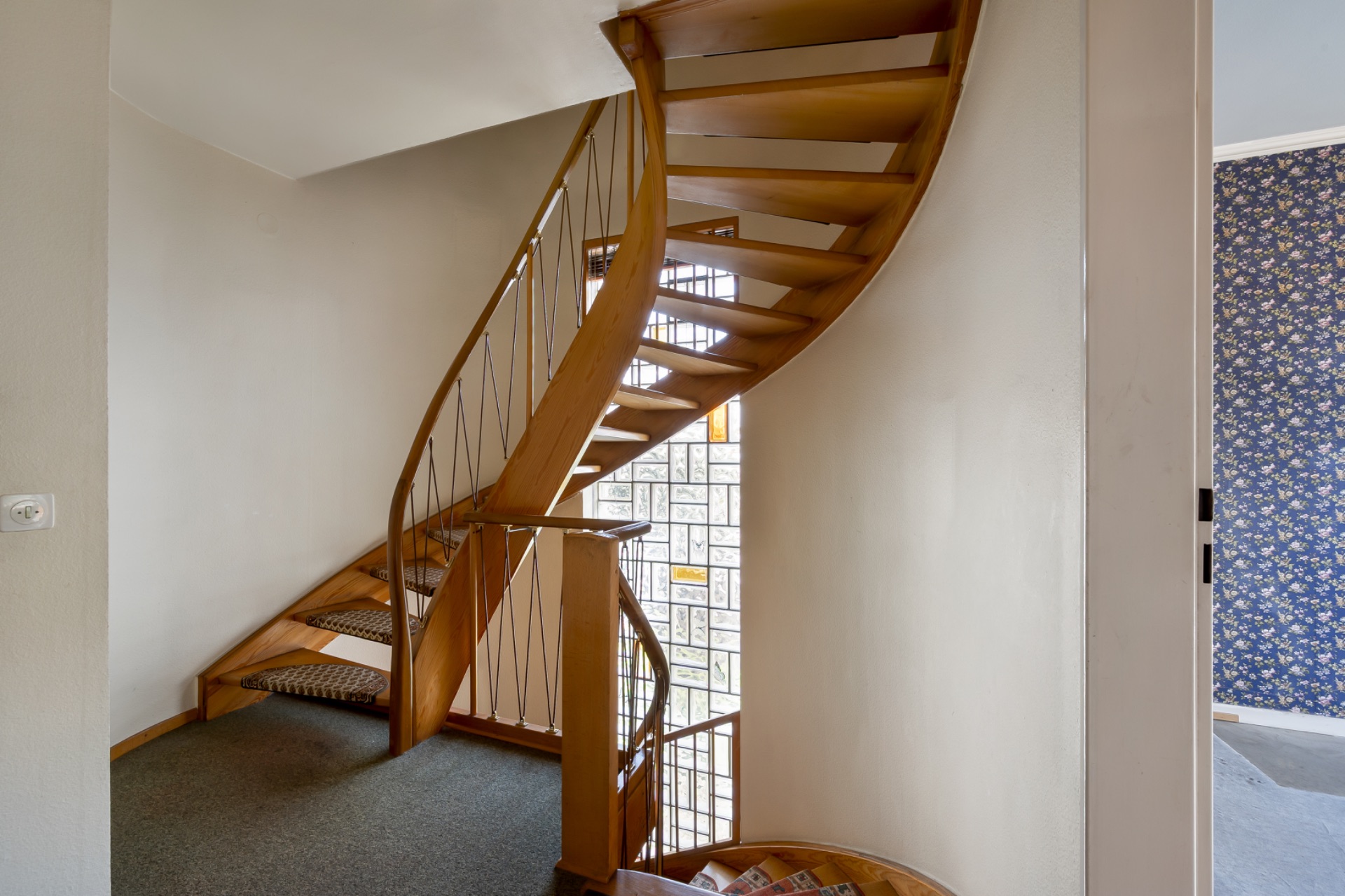 Holztreppe mit Metallgeländer in einem Wohnhaus, daneben Fenster mit Glasbausteinen.