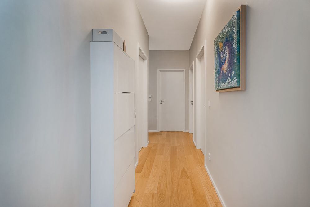 Heller Flur mit Holzboden, weißem Schrank und Wandbild an der rechten Wand.