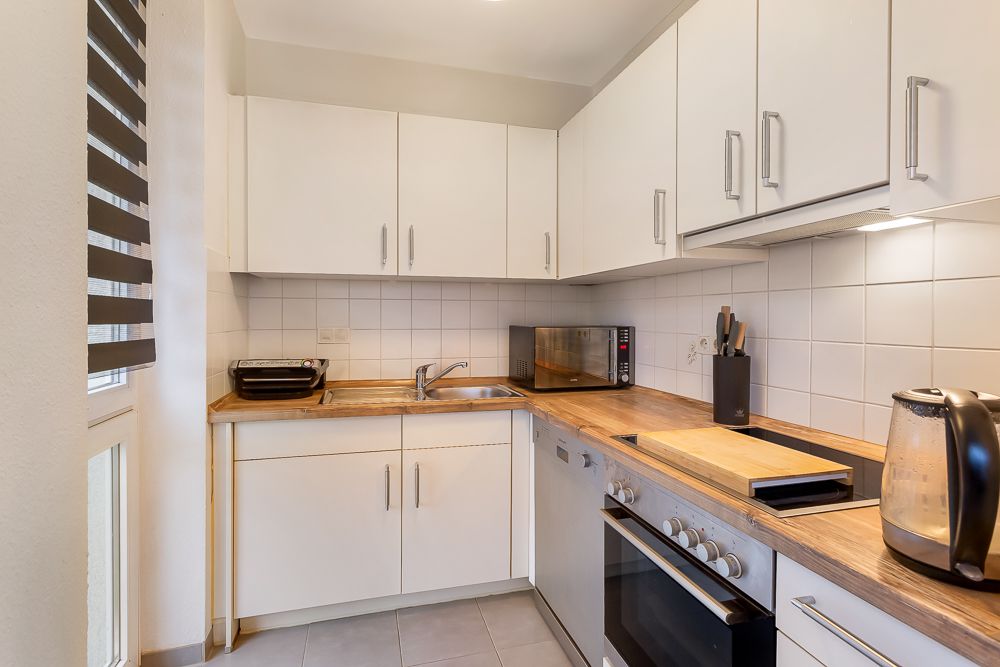 Moderne Küche mit weißen Schränken, Holzarbeitsplatte, Backofen und Küchenutensilien.