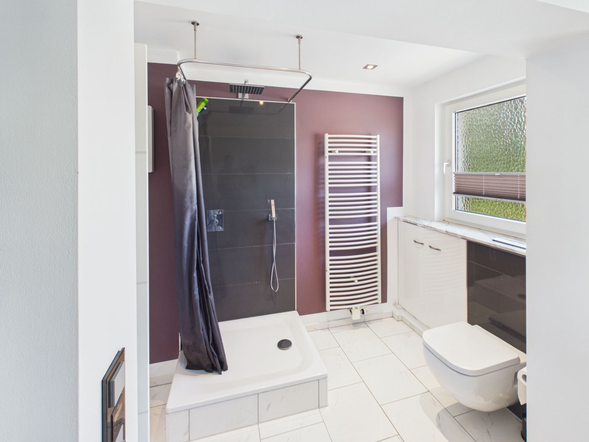 Modernes Badezimmer mit Dusche, Handtuchheizkörper, Fenster und Toilette.