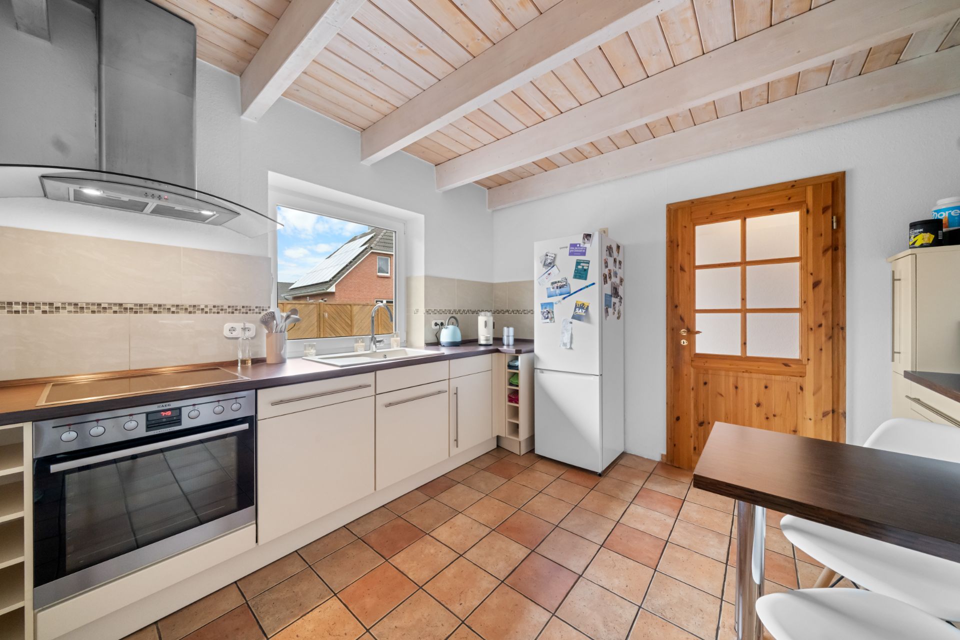 Moderne Küche mit Einbauherd, Kühlschrank, Fenster und Holzbalkendecke.