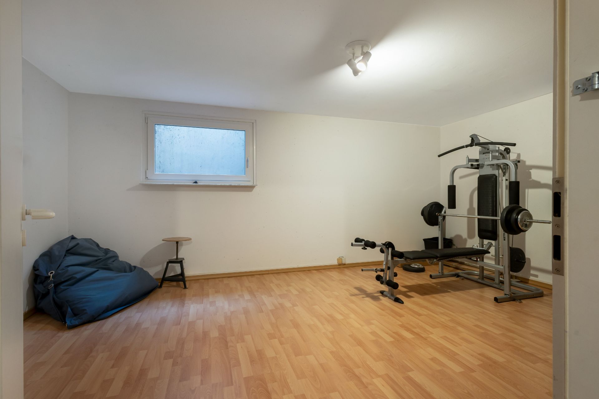 Heller Raum mit Holzfußboden, Kraftstation, Sitzsack und Hocker, Fenster an der Wand.