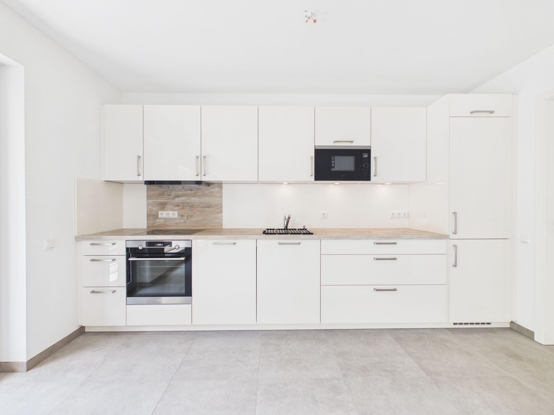 Moderne weiße Einbauküche mit Backofen, Herd, Mikrowelle und Oberschränken.