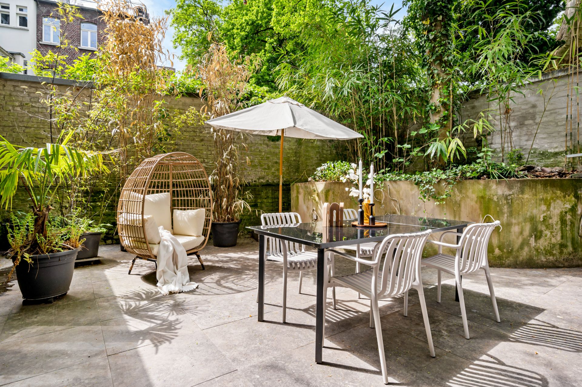 Garten mit Esstisch, Stühlen, Sonnenschirm, Korbsessel und vielen Pflanzen.