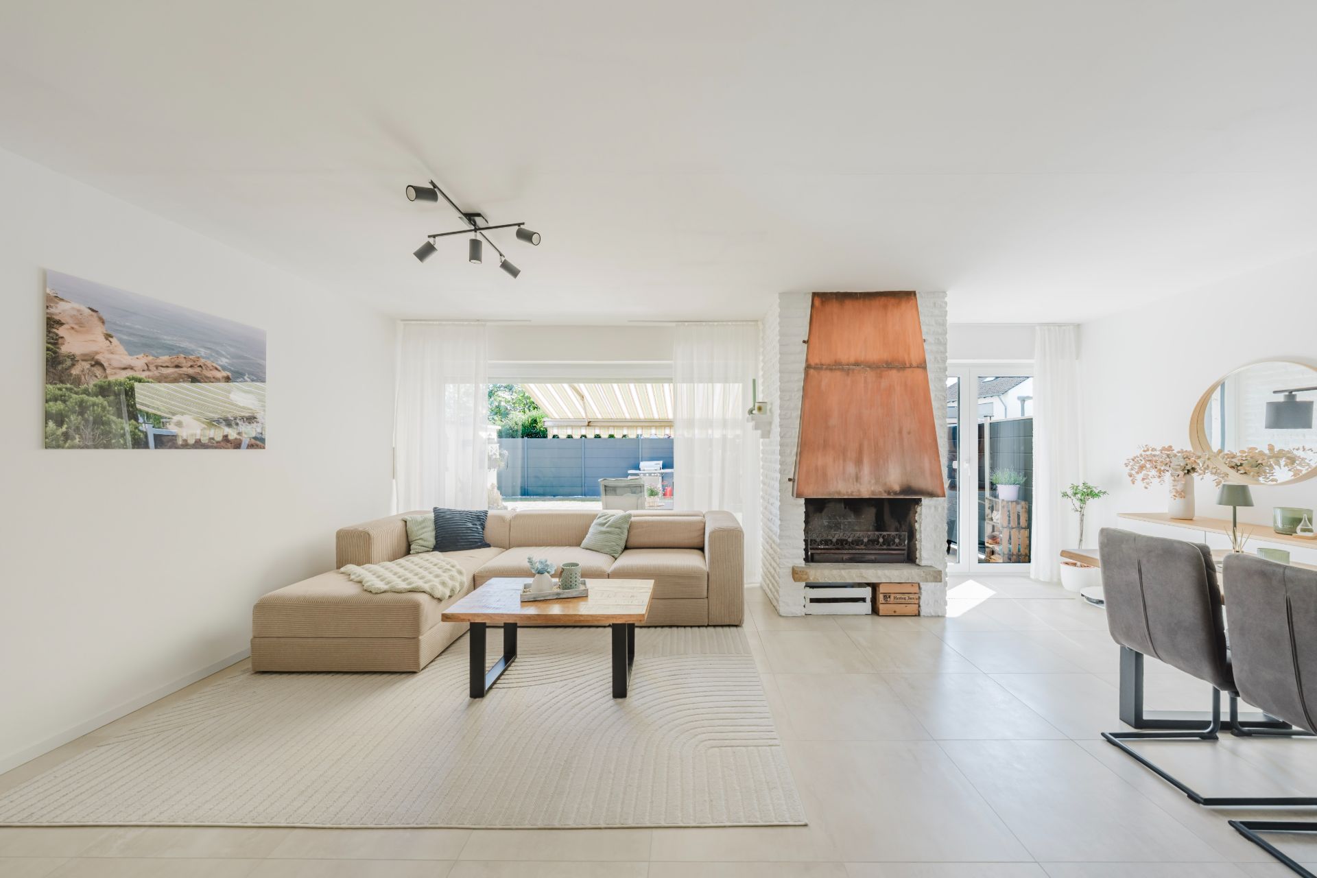 Helles Wohnzimmer mit Ecksofa, Couchtisch, Kamin und Esstisch mit Stühlen.