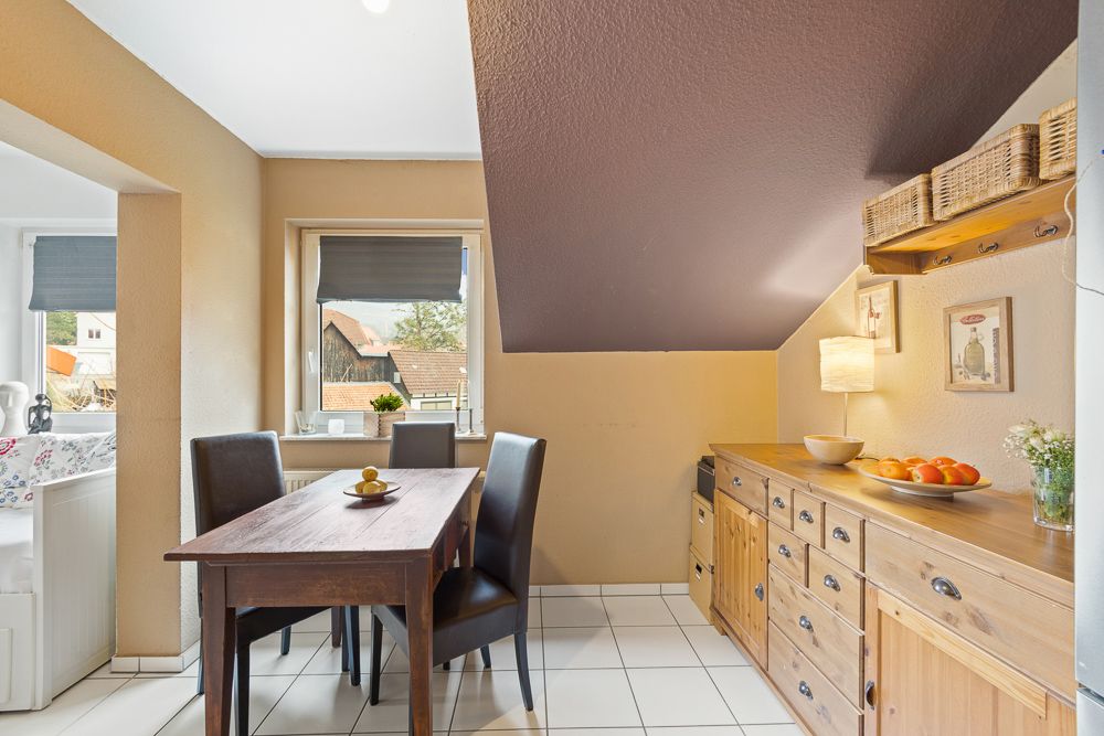 Essbereich mit Holztisch, vier Stühlen, Kommode, Obstschale und Fenster mit Blick nach draußen.