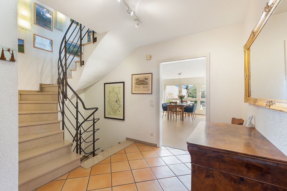 Heller Flur mit Treppe, Kommode, Wandbildern und Blick ins Esszimmer.