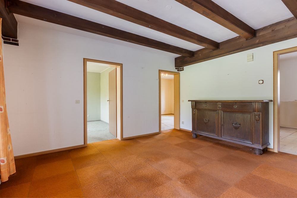 Zimmer mit braunem Teppich, Holzbalken an der Decke und dunklem Holzschrank.