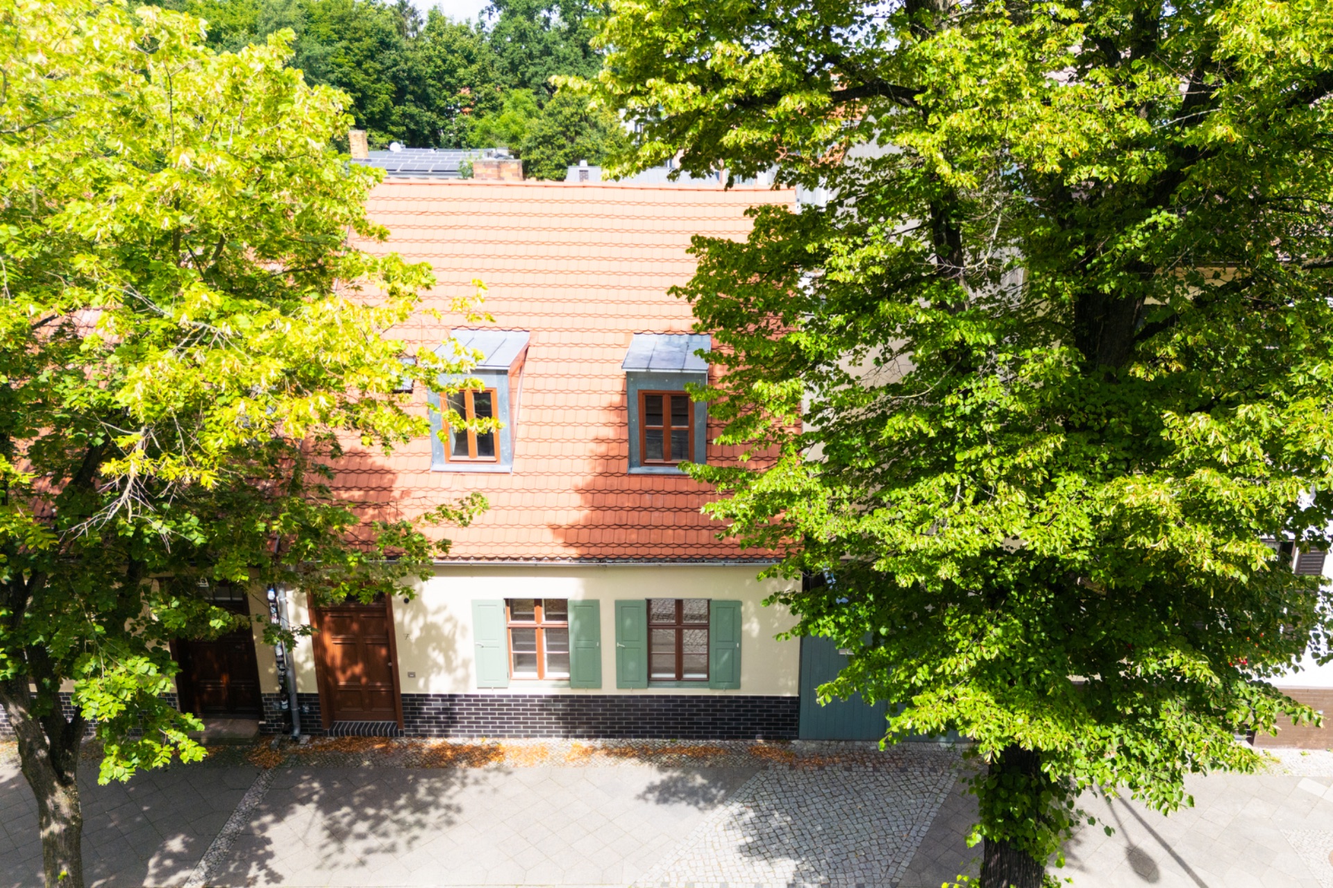 Zweistöckiges Wohnhaus mit rotem Dach und Bäumen im Vordergrund.